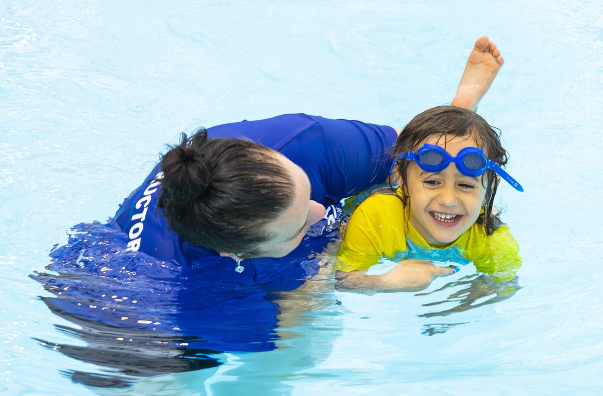 Kāpiti Aquatics swim instructor teaching a young child to kick their legs